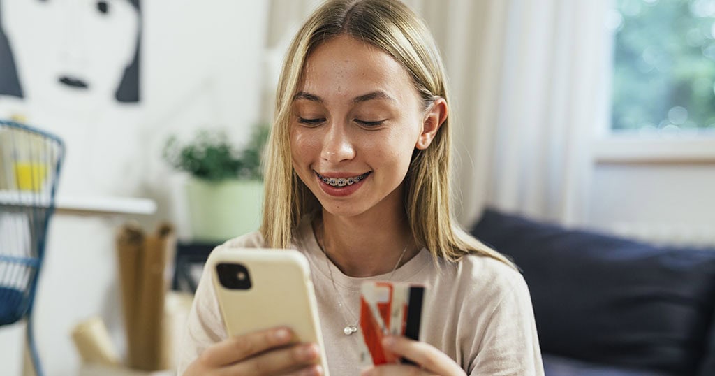 Adolescente faisant des achats en ligne à l'aide de son téléphone portable et sa carte de crédit