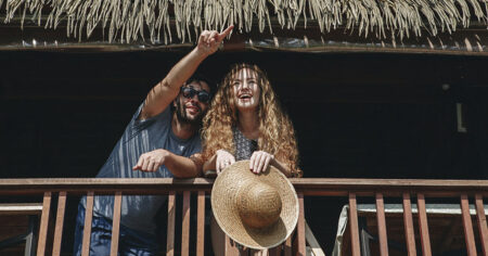 Un homme et une femme sur un balcon en bois sous un toit en chaume, l'homme pointant quelque chose au loin